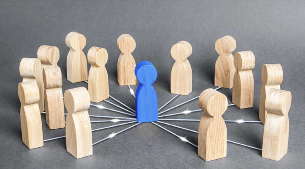 a graphic of wooden figurines, with one blue figurine in the middle of a circle of beige figurines. there are white lines connecting them all at the base.