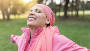 a woman wearing all pink and a pink headscarf is standing outside. she has her arms outstretched and is smiling. her head is pointed upwards.