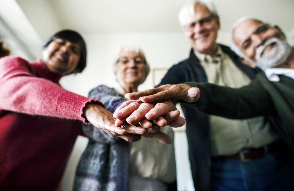 a group of elderly people are staring down at the camera, with their hands piled on top of each other in the centre. their faces are blurry, but they are all smiling.